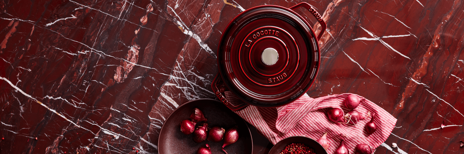 Grenadine Staub Dutch oven on a burgundy, marble counter.